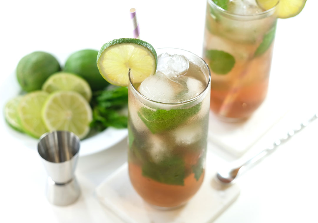 elderberry-mojito-benefits 2 elderberry tea mojitos sitting on coasters next to a plate of limes and mint
