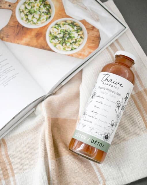 bottle of thrive remedies detox flavour sitting on a kitchen towel next to a cookbook