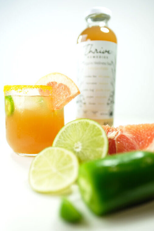 spiced paloma cocktail next to a lime, grapefruit and jalapeno