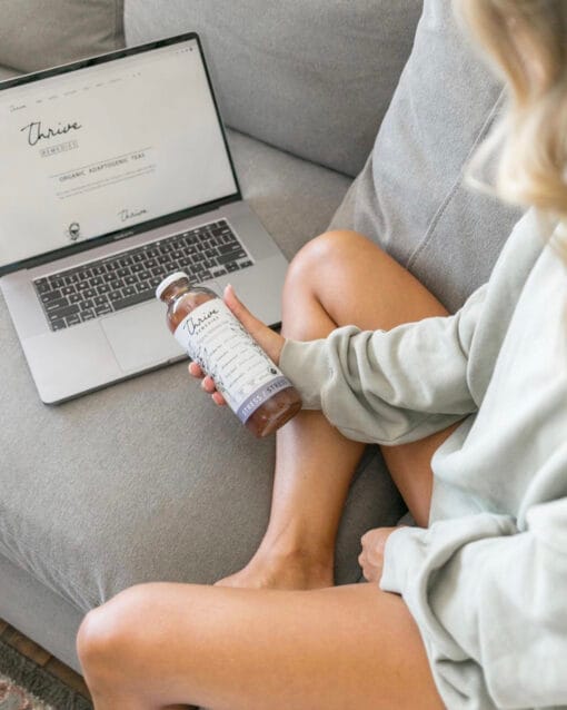 woman sitting on the couch with her laptop holding a bottle of thrive remedies stress flavour
