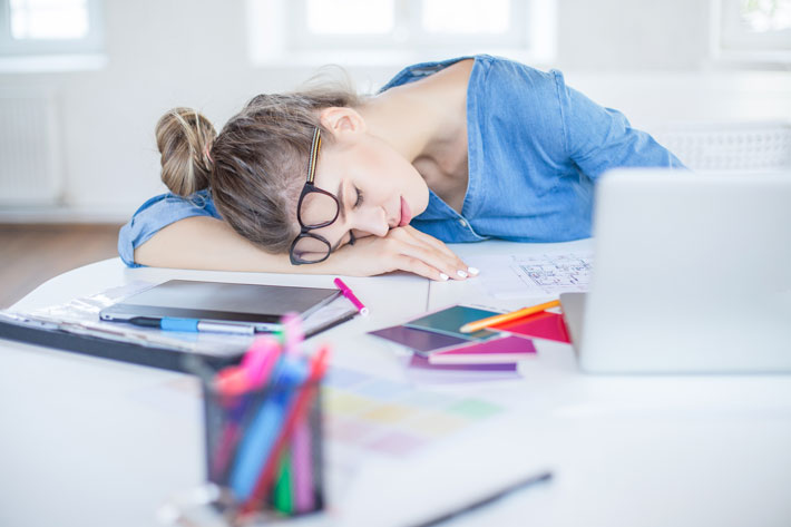 woman sleeping at her work desk on piles of paperwork