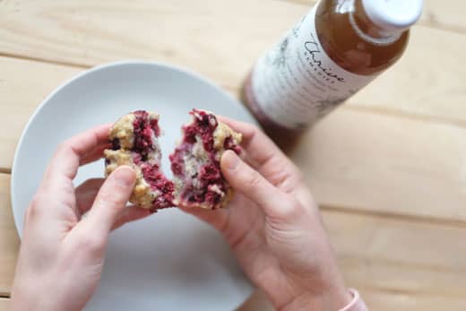 persons hands breaking apart a raspberry muffin with a bottle of tea in front of them